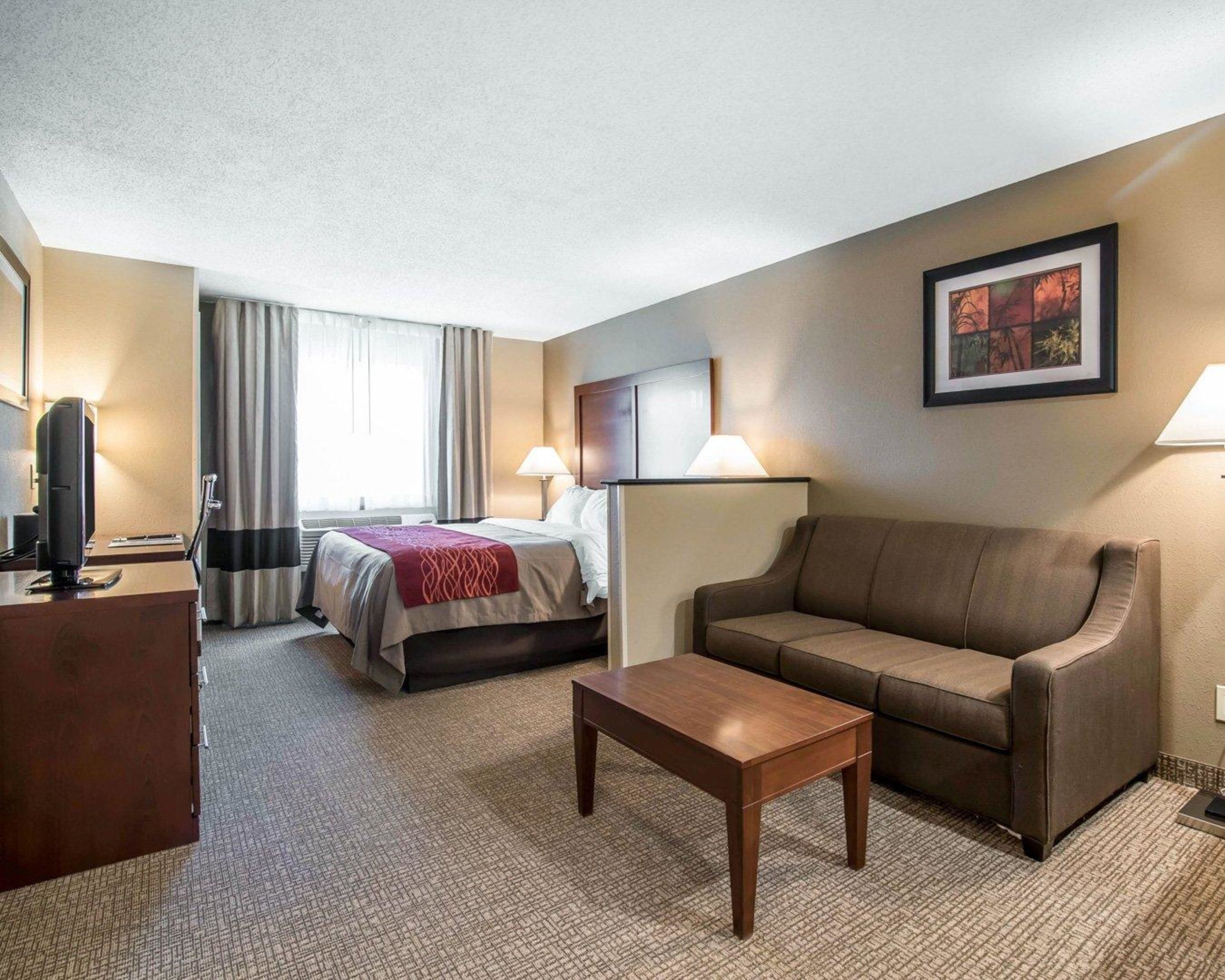 Una habitación de hotel con cama, sofá, mesa de centro, escritorio y televisión.