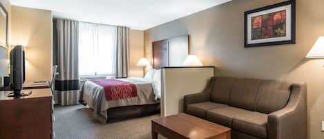 Una habitación de hotel con cama, sofá, mesa de centro, escritorio y televisión.