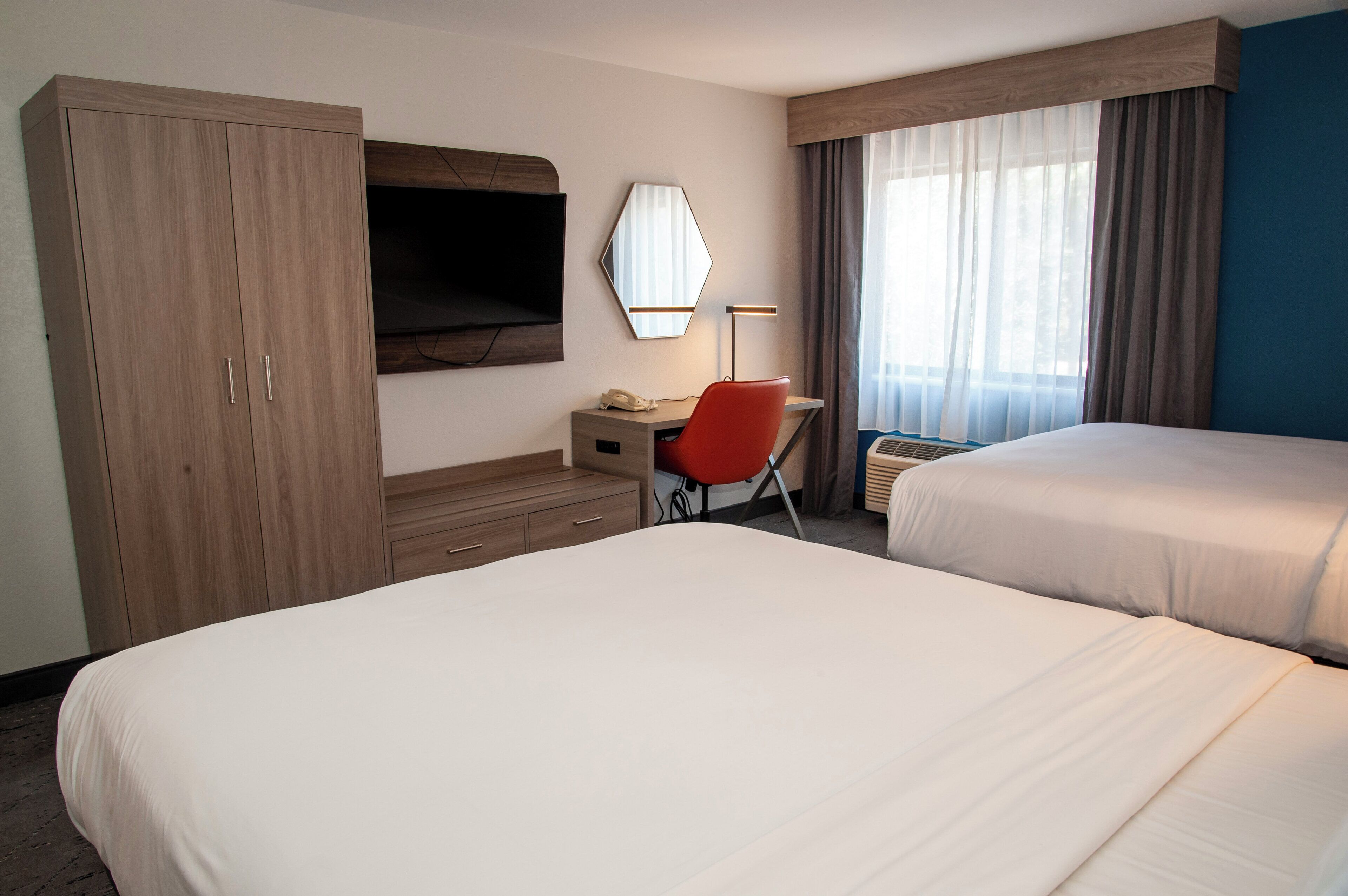 A hotel room with two beds, a desk with a chair, a TV, and a large wardrobe.