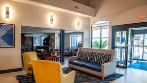 A lobby with a sofa, yellow armchair, and a dining area with chairs and tables. - Holiday Inn Express Airport - Tucson by IHG (Tucson)