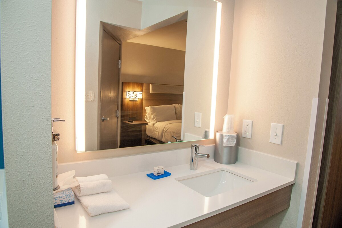 A hotel bathroom with a large mirror, a sink, a towel rack, and a toilet.
