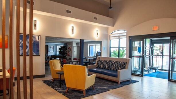 A spacious lobby with a sofa, chairs, and a coffee table. There is a reception desk and a door leading outside. - Holiday Inn Express Airport - Tucson by IHG (Tucson)