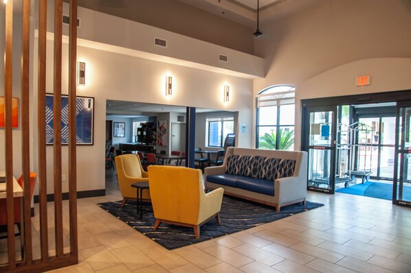 A spacious lobby with a sofa, chairs, and a coffee table. There is a reception desk and a door leading outside. - Holiday Inn Express Airport - Tucson by IHG (Tucson)