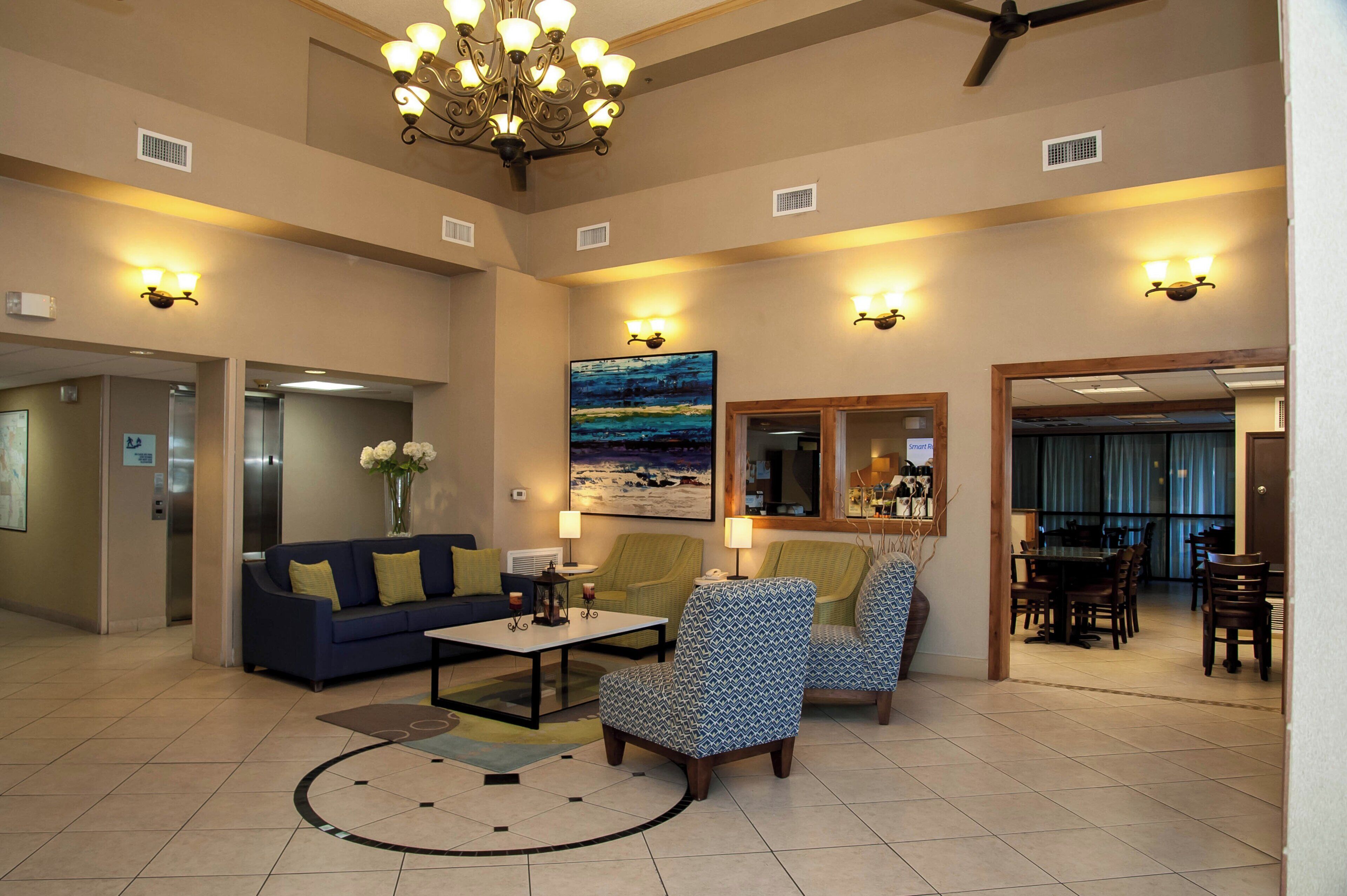 A spacious lobby with a chandelier, seating area, artwork, and a view into the dining area.