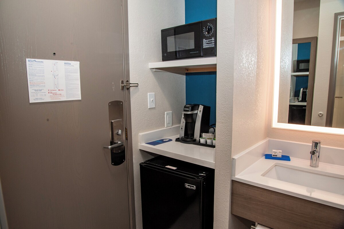 A compact hotel bathroom with a microwave, coffee maker, and a small refrigerator.