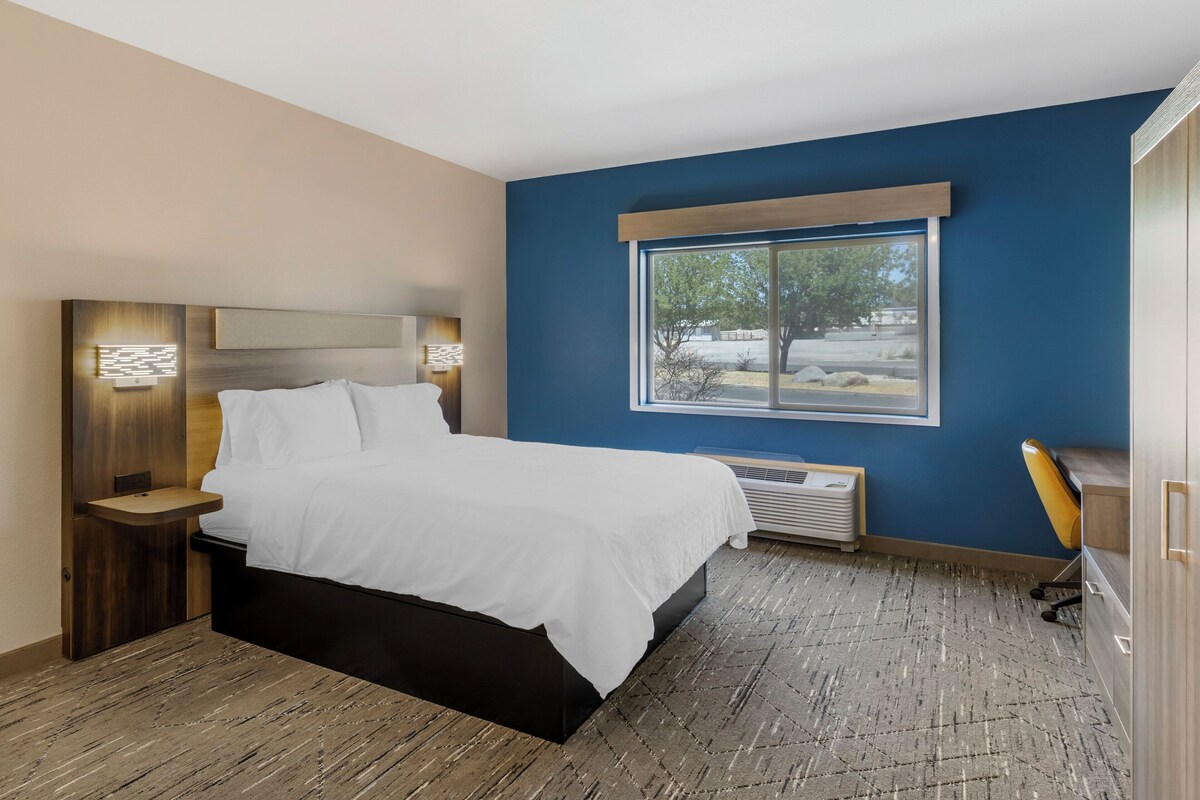 A modern hotel room with a large bed, bedside tables, a desk, and a window with a view of the outdoors.