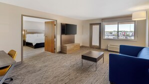 A hotel room with a bed, a TV, a blue sofa, a small table, and a view of the outside through a window.