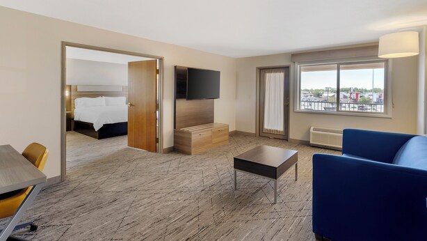 A hotel room with a bed, a TV, a blue sofa, a small table, and a view of the outside through a window.
