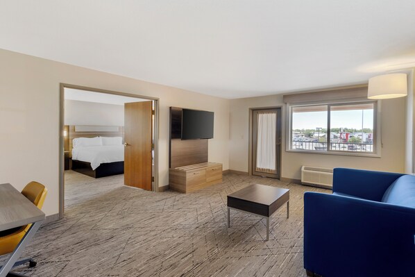 A hotel room with a bed, a TV, a blue sofa, a small table, and a view of the outside through a window. - Holiday Inn Express Fallon by IHG (Fallon)