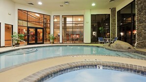 An indoor swimming pool with a hot tub, surrounded by a stone wall and glass doors leading to a dining area.