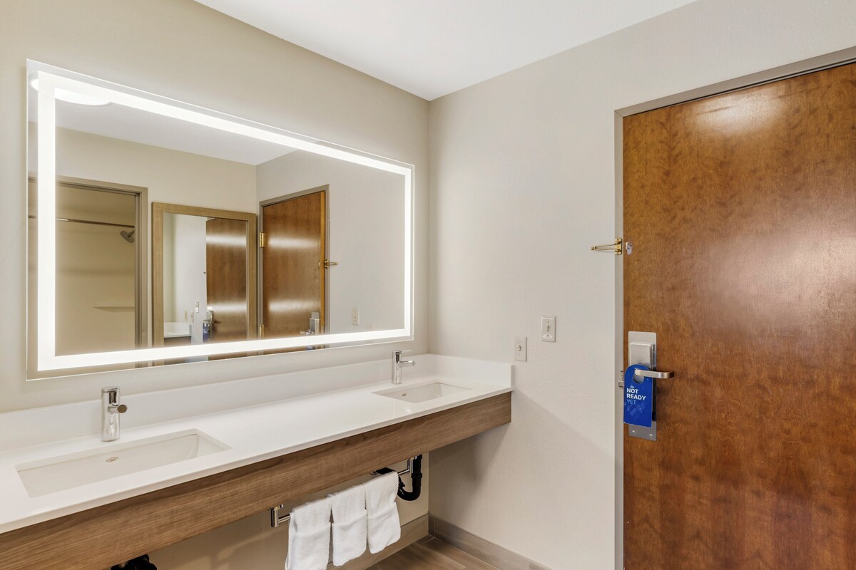 A modern bathroom with a large mirror, two sinks, and a wooden door.