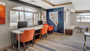 A modern hotel room with a desk, two orange chairs, a large window, and a wall with abstract art.