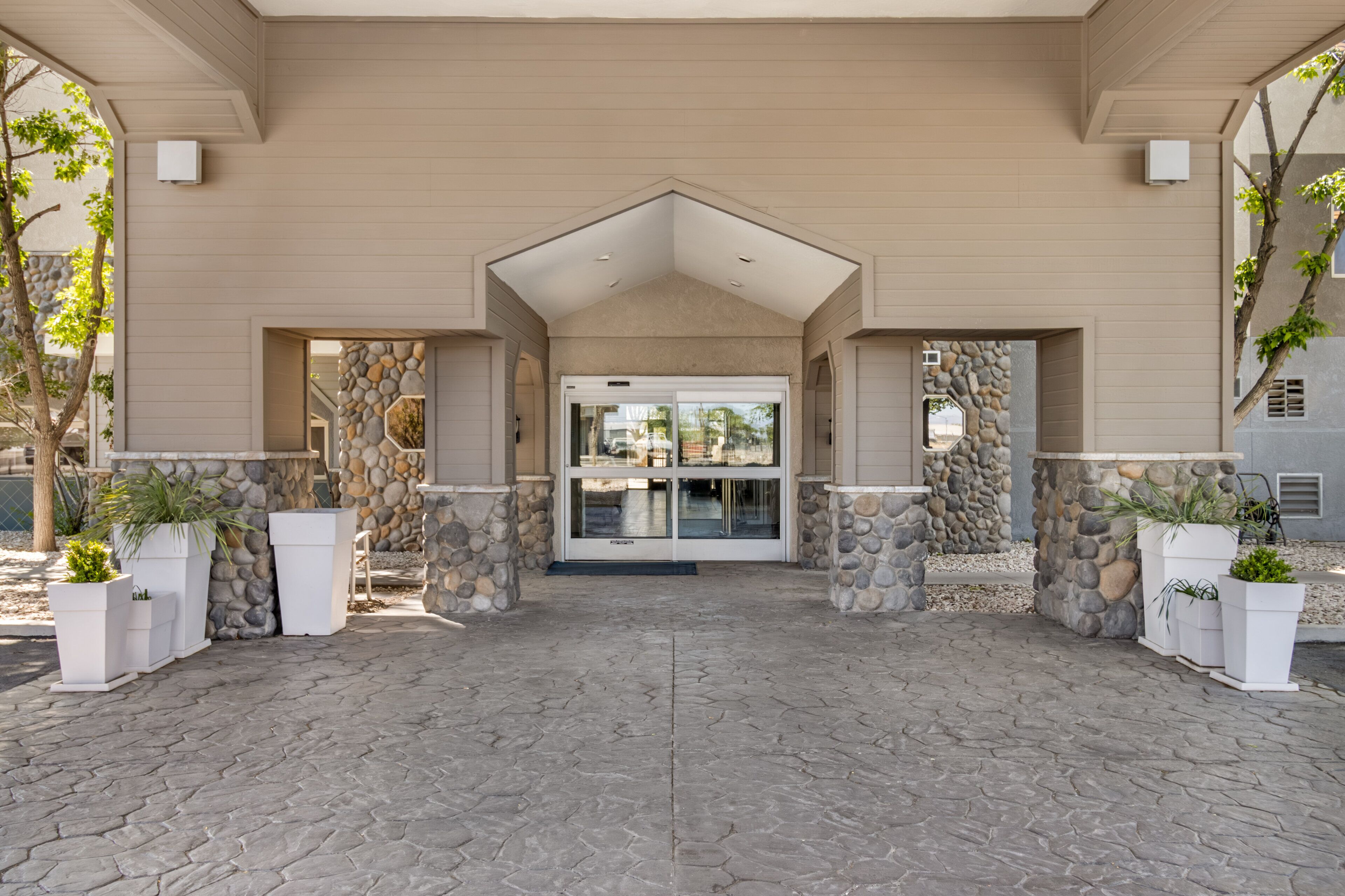 A building entrance with a stone facade, a covered walkway, and potted plants.