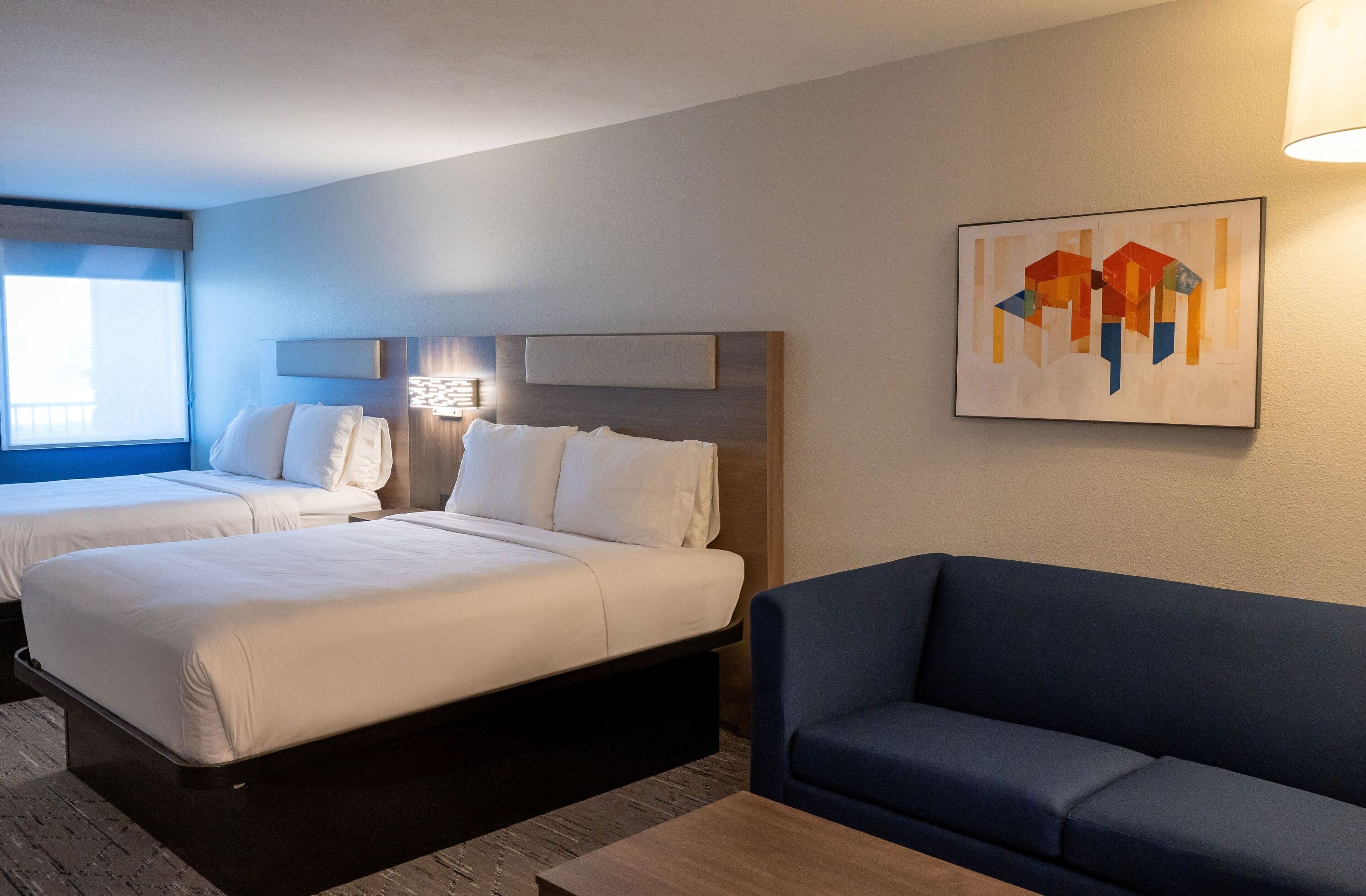 A hotel room with two beds, a sofa, and a painting on the wall.