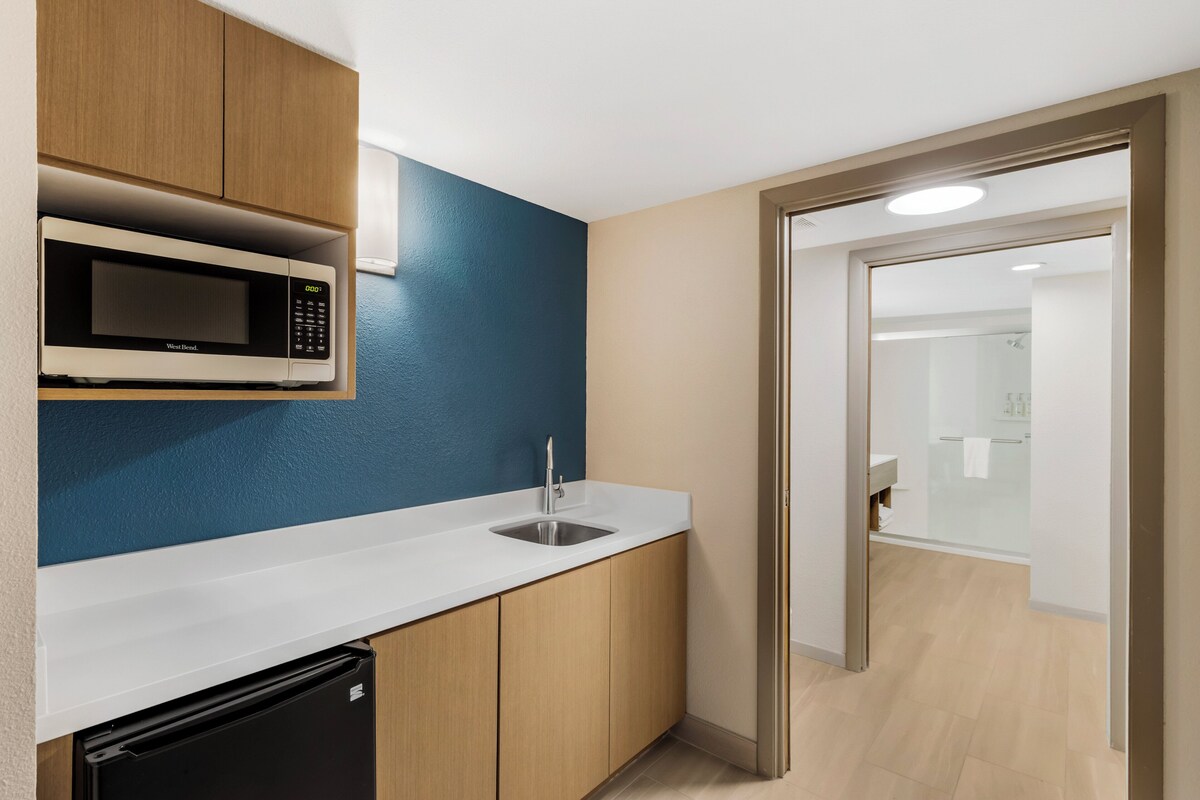 A compact kitchen with a microwave, sink, and dishwasher, and a door leading to a bathroom.