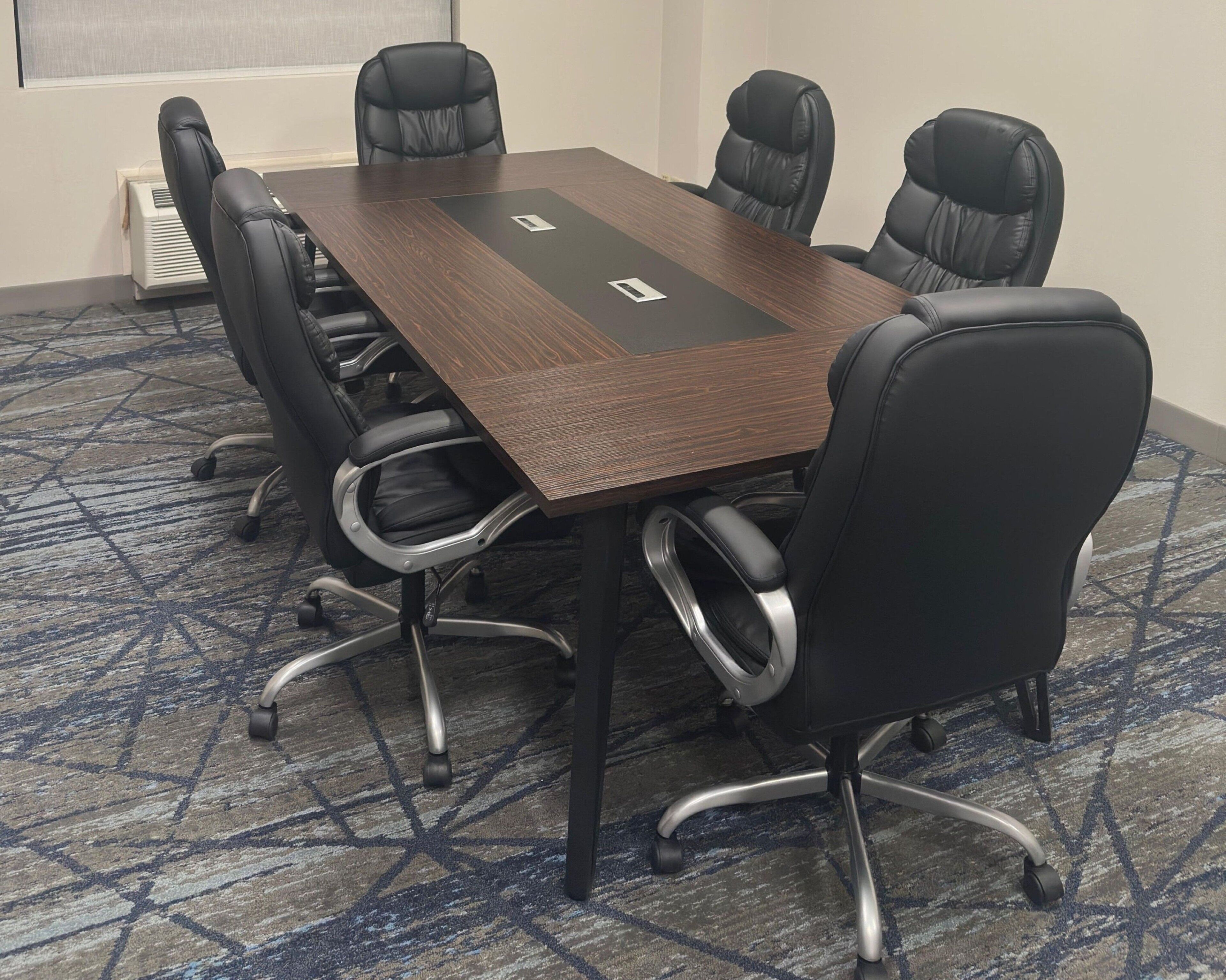 A conference room with a dark wooden table, black leather chairs, and a patterned carpet.