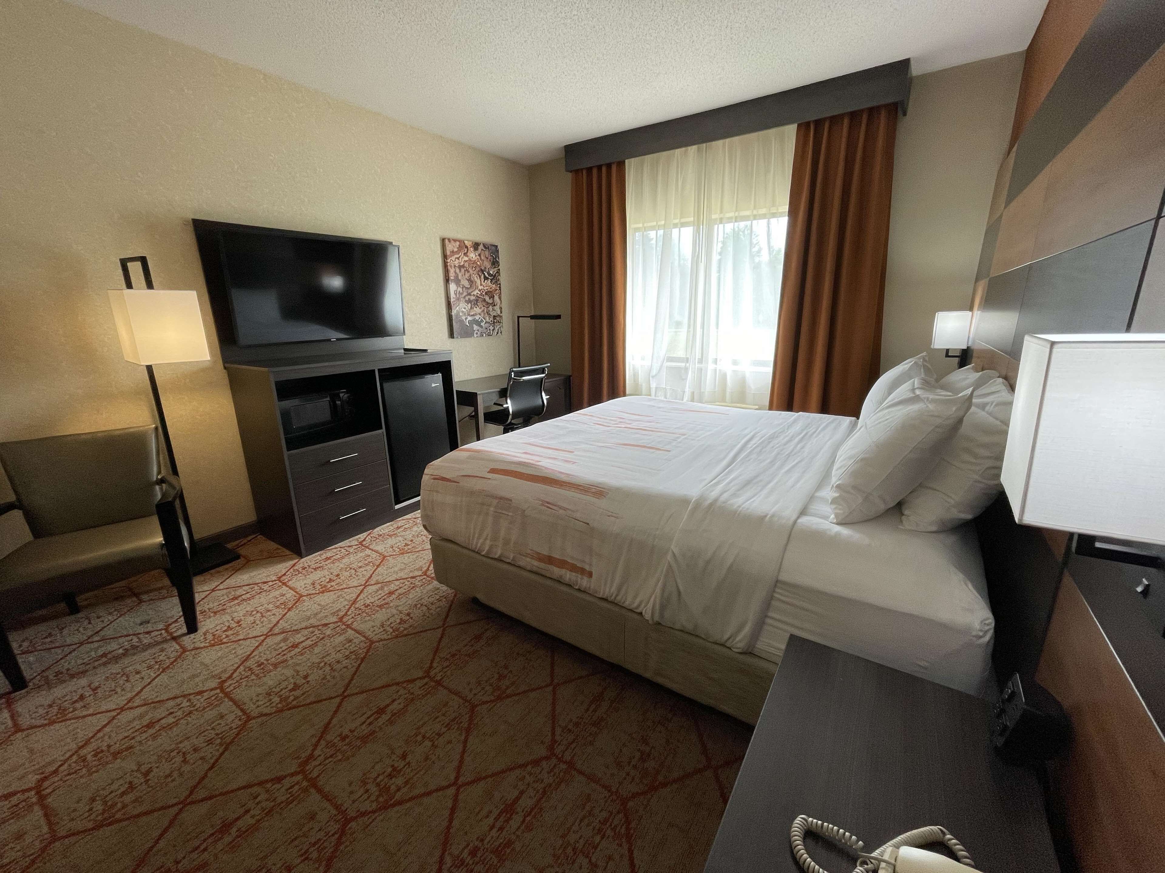 A hotel room with a bed, desk, chair, television, and a window with curtains.