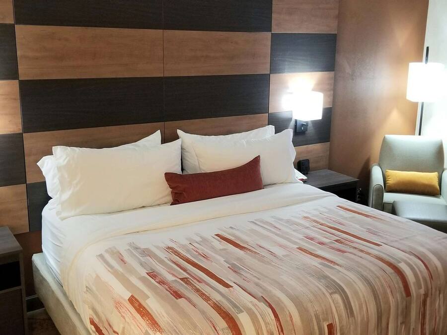 Een hotelkamer met een groot bed, twee nachtkastjes, een stoel en een lamp.