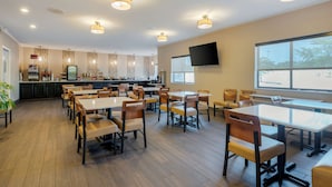 A spacious dining area with multiple tables and chairs, a kitchen in the background, and a large window providing natural light. - Best Western Plus Warsaw (Warsaw)