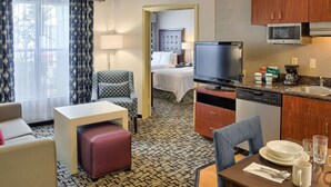 A hotel room with a bed, a TV, a dining area with a table and chairs, a kitchen with a microwave, and a patterned floor. - Homewood Suites by Hilton Mobile Airport-University Area (Mobile)