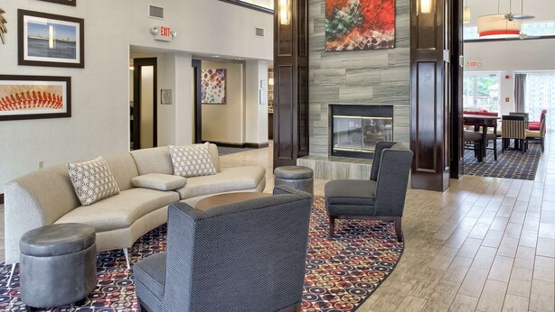 A lobby with a sofa, armchairs, a patterned rug, and a fireplace. - Homewood Suites by Hilton Mobile Airport-University Area (Mobile)