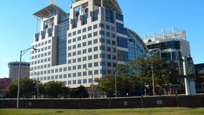 A modern multi-story building with a distinctive architectural design, featuring a central tower and a curved glass facade. - Homewood Suites by Hilton Mobile Airport-University Area (Mobile)