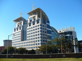 Un edificio moderno de varios pisos con un diseño arquitectónico distintivo, que presenta una torre central y un frente de cristal curvo.