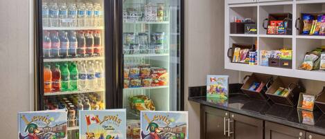A hotel lobby with a snack bar, a refrigerator stocked with beverages, and a display of children's books.