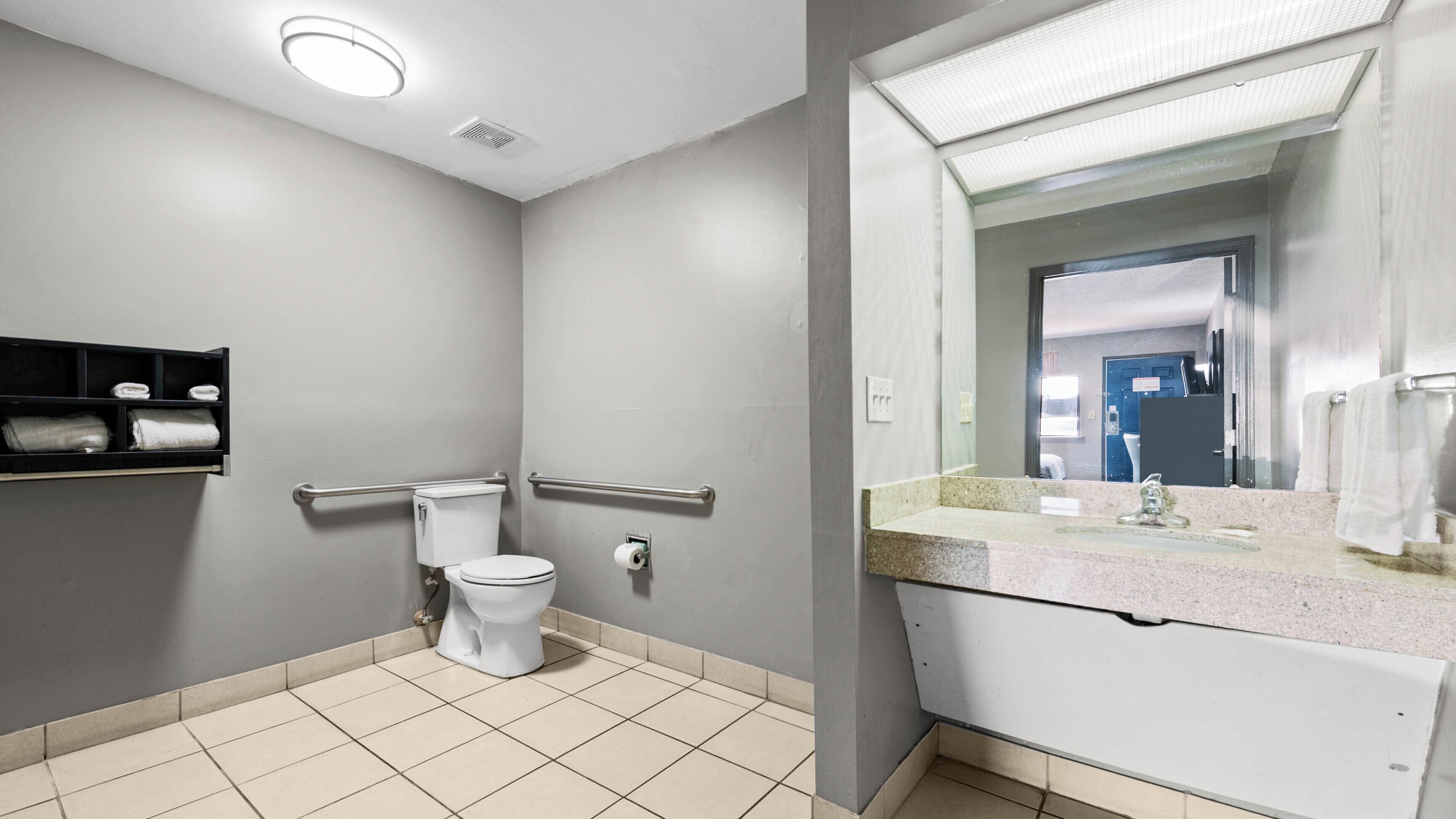 A bathroom with a toilet, handrails, a sink, and a mirror.