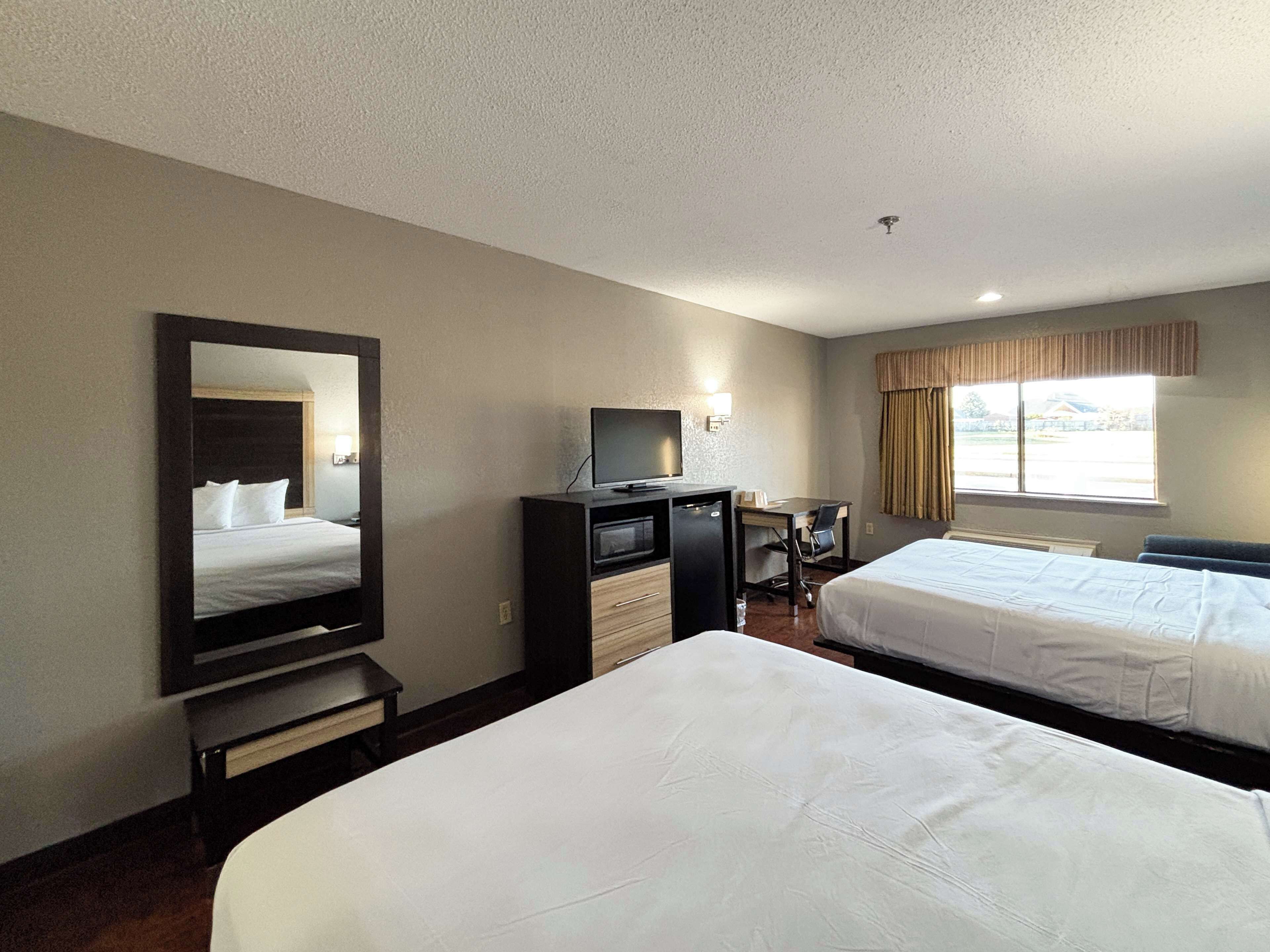 A hotel room with two beds, a desk with a computer, a TV, and a large mirror.