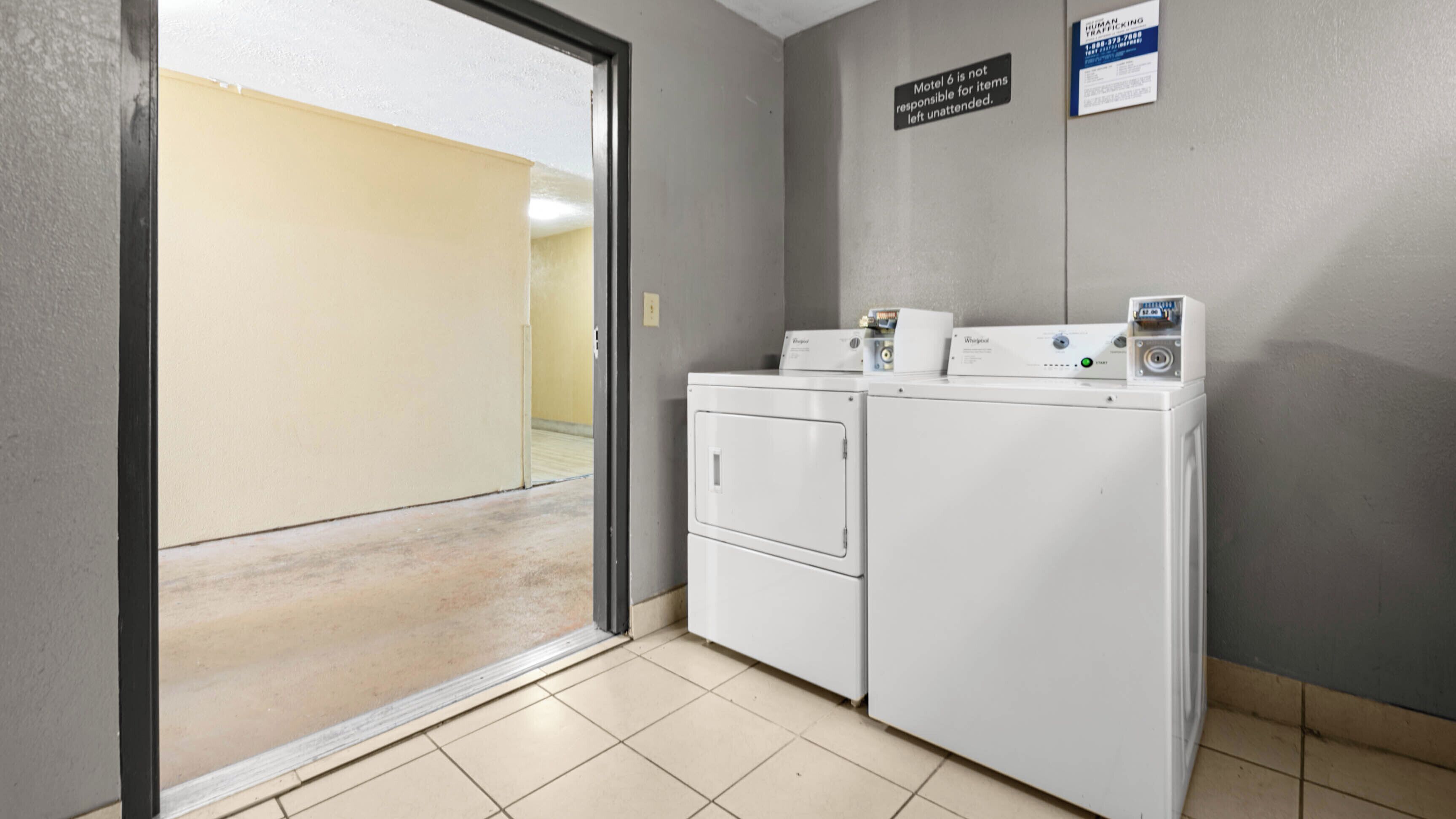 A laundry room with two Whirlpool washers and dryers, a sign indicating Motel 6 is not responsible for unattended items, and a human trafficking awareness sign.