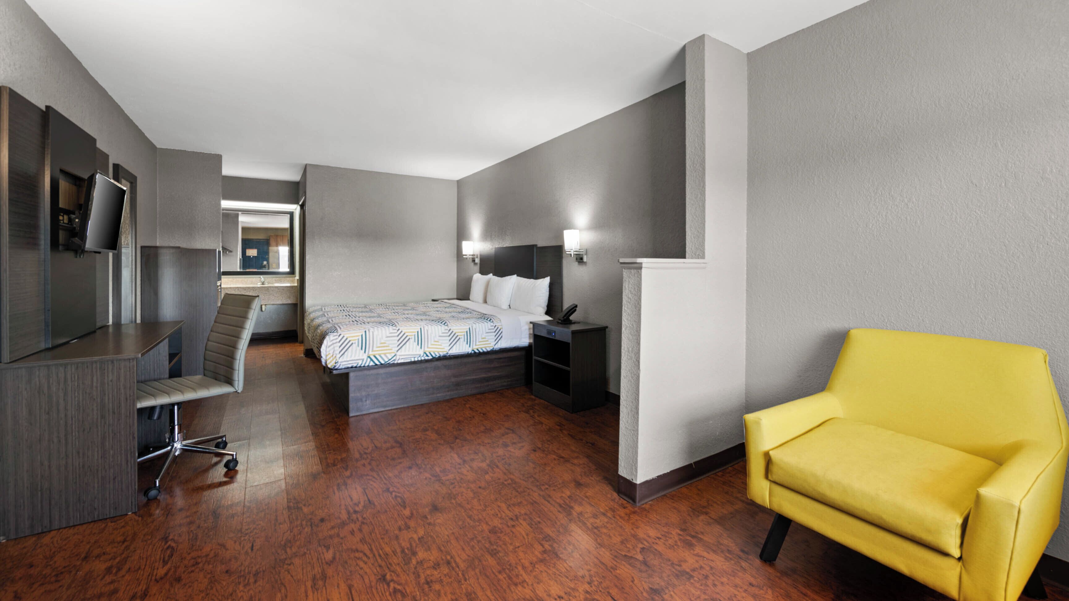 Una habitación de hotel con una cama, un escritorio, una silla, un televisor y un espejo.