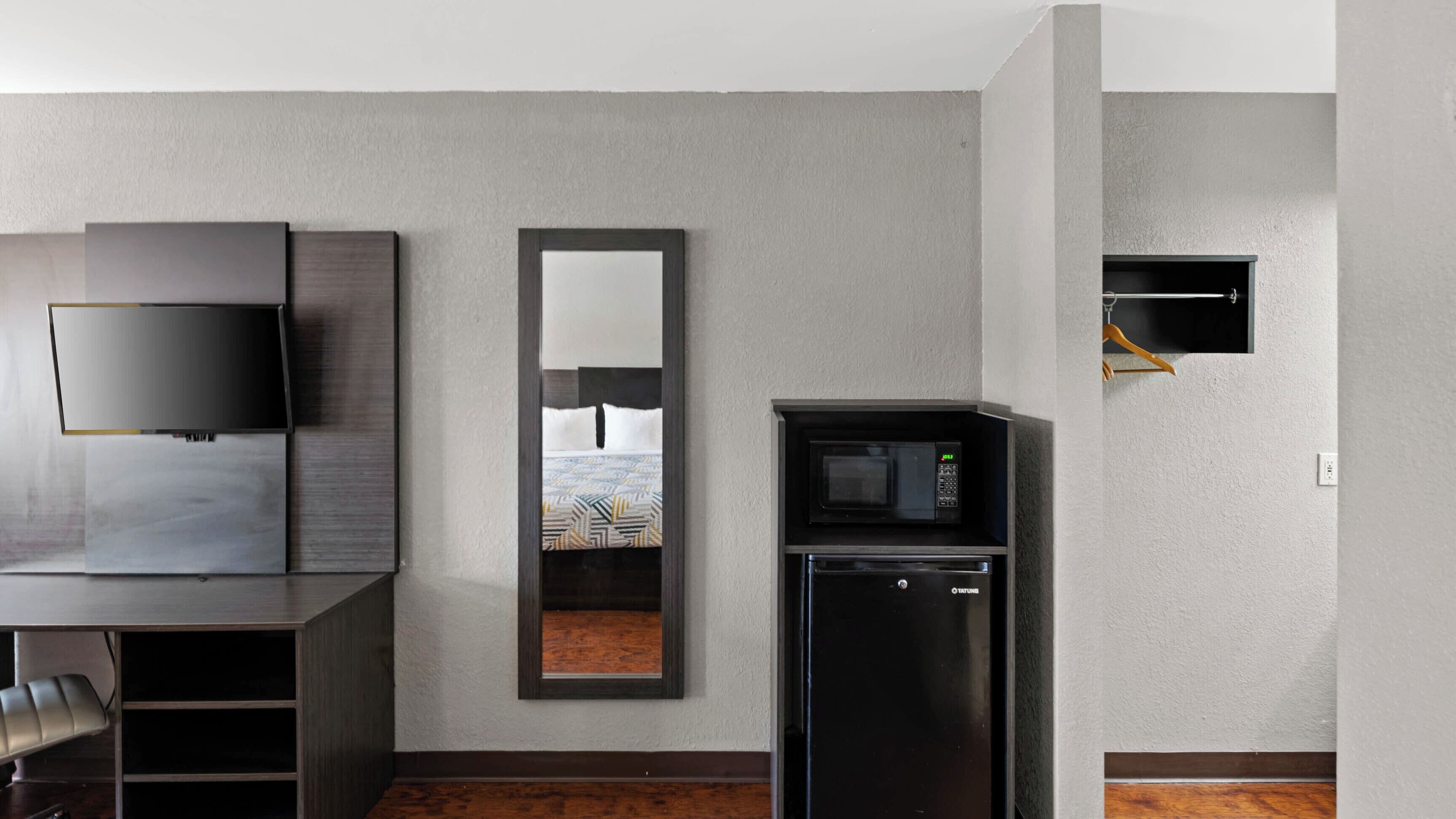 A hotel room with a flat-screen TV, a mirror, a refrigerator, and a microwave.