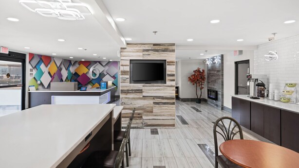 A modern kitchen with a flat-screen TV, a coffee machine, and a seating area with a table and chairs. - Motel 6 Prattville, AL (Prattville)