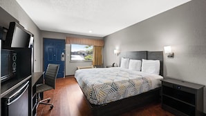 A hotel room with a bed, a desk with a flat-screen TV, a chair, a window with curtains, and a view of the cityscape. - Motel 6 Prattville, AL (Prattville)