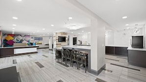 A modern hotel lobby with a reception desk, bar area, and seating. - Motel 6 Prattville, AL (Prattville)