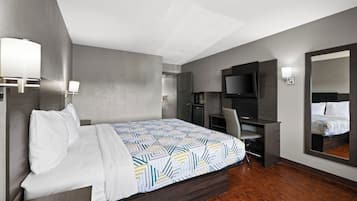 A hotel room with a bed, a desk, a chair, a TV, and a mirror.