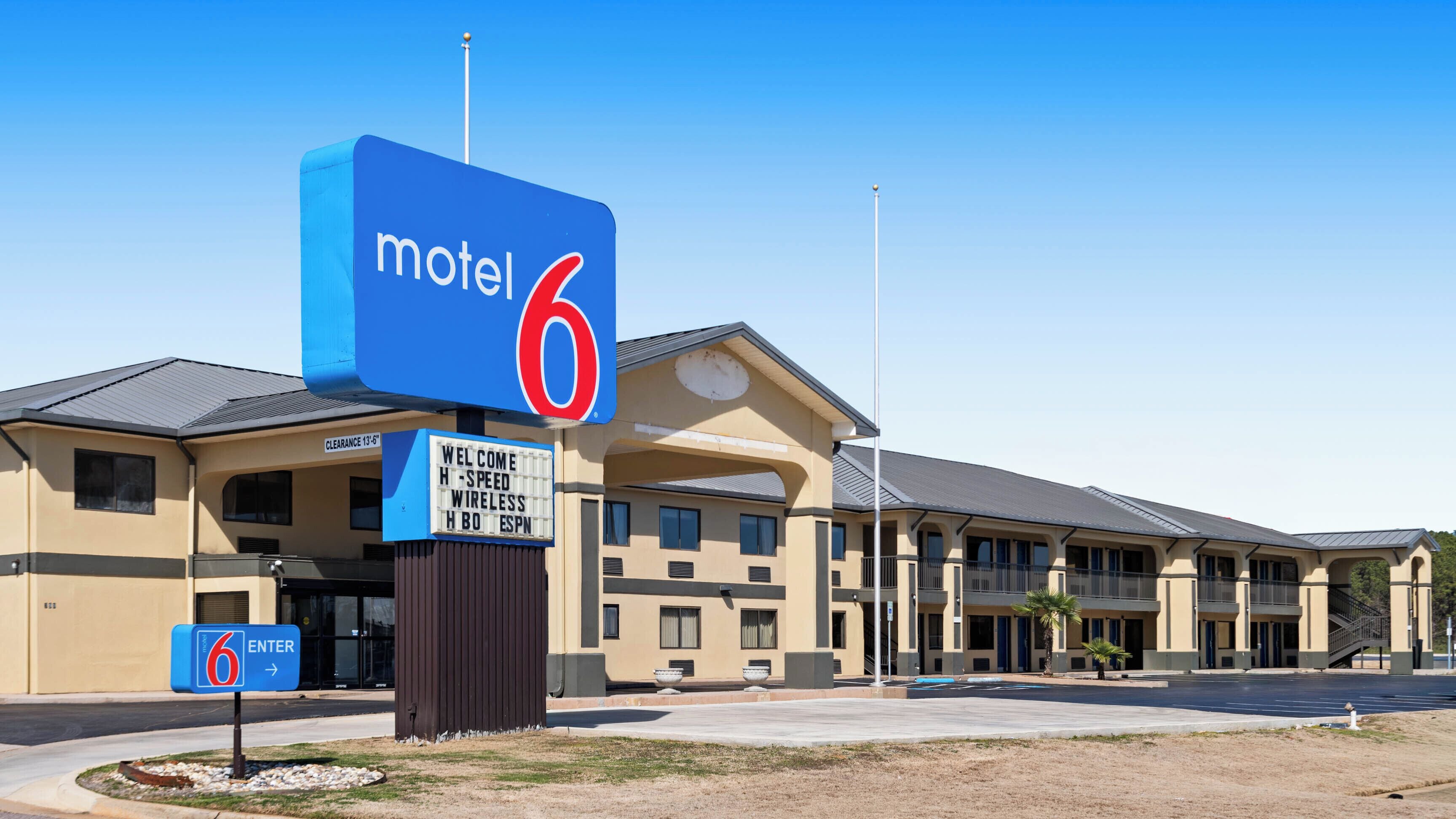 A motel with a large blue sign, a welcome message, and a clear sign indicating the entrance.