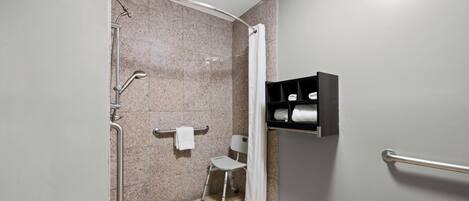 A shower area with a grab bar, a towel rack, and a shelf with towels.