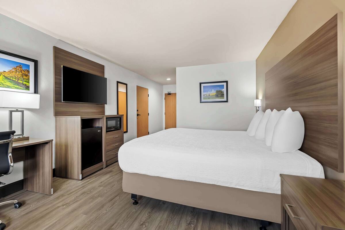 Une chambre d’hôtel moderne dotée d’un grand lit, d’un bureau avec une chaise, d’un téléviseur à écran plat et d’un autre téléviseur placé sur une commode en bois.