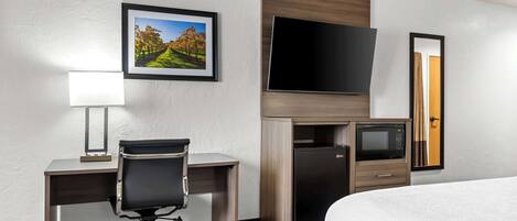 A hotel room with a bed, a desk with a chair, a television, a microwave, and a refrigerator.