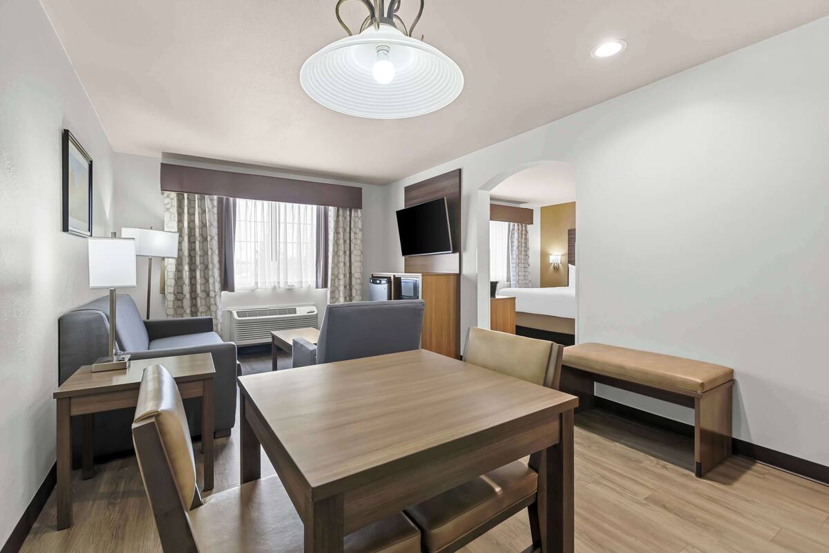Une chambre d’hôtel comprenant un coin repas, un canapé, une télévision et une fenêtre avec des rideaux.