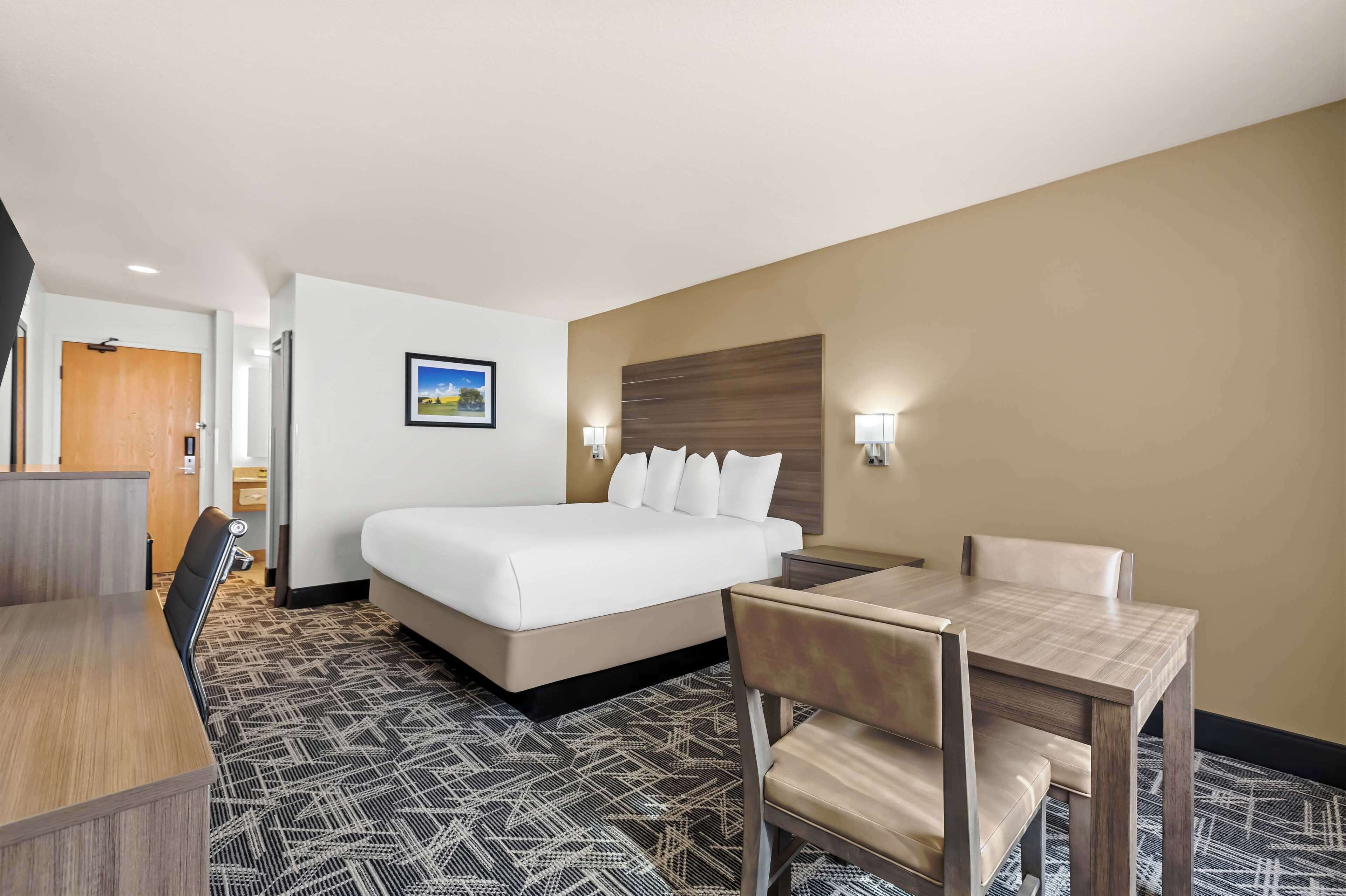 A hotel room with a bed, a desk, a chair, a table, and a picture on the wall.