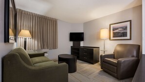 Een hotelkamer met een groene bank, een bruine leren fauteuil, een flatscreen televisie, een bureau met een lamp en een ingelijst schilderij aan de muur.