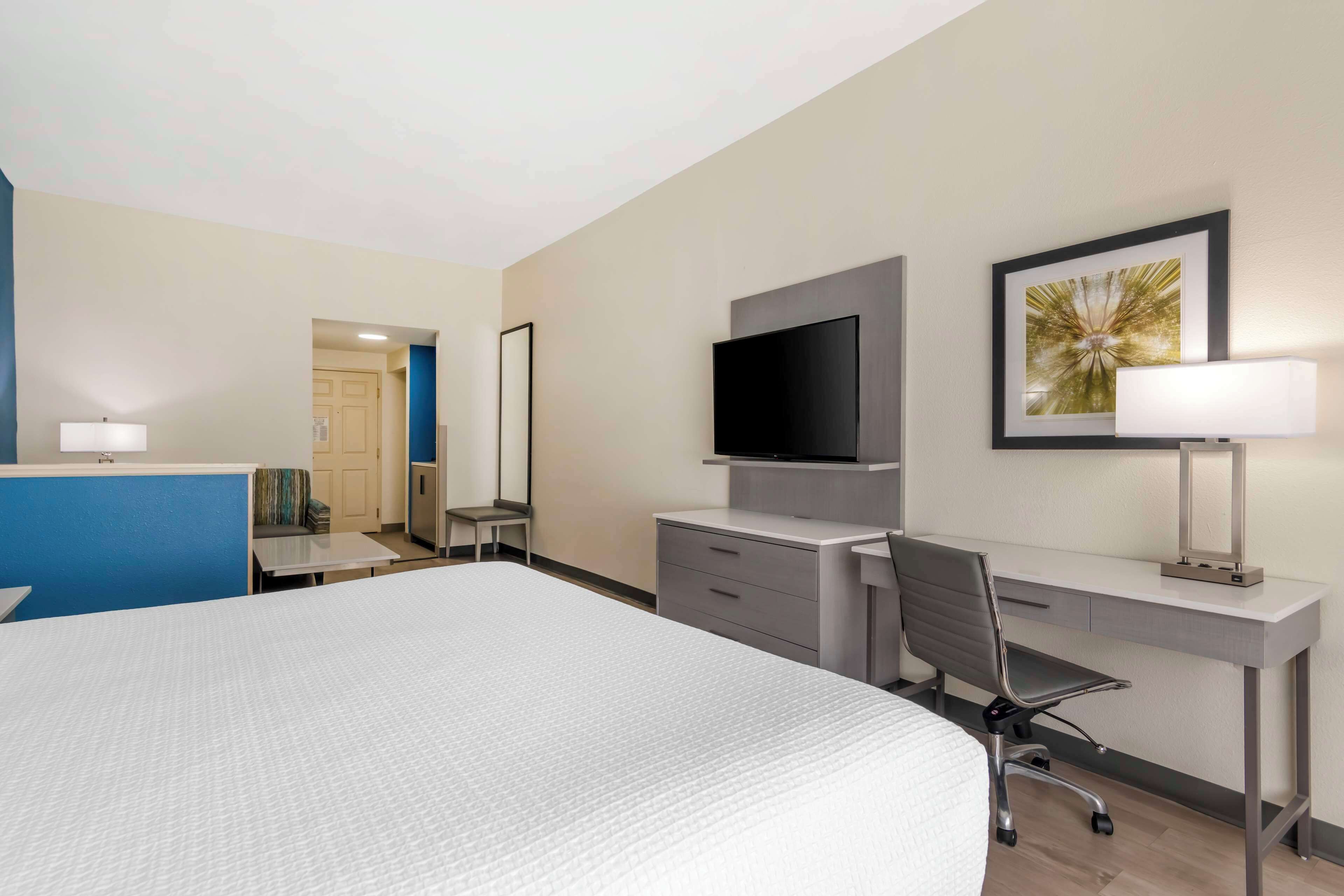 Habitación de hotel con una cama grande, un escritorio con silla, un televisor de pantalla plana, una lámpara de escritorio y un cuadro en la pared.