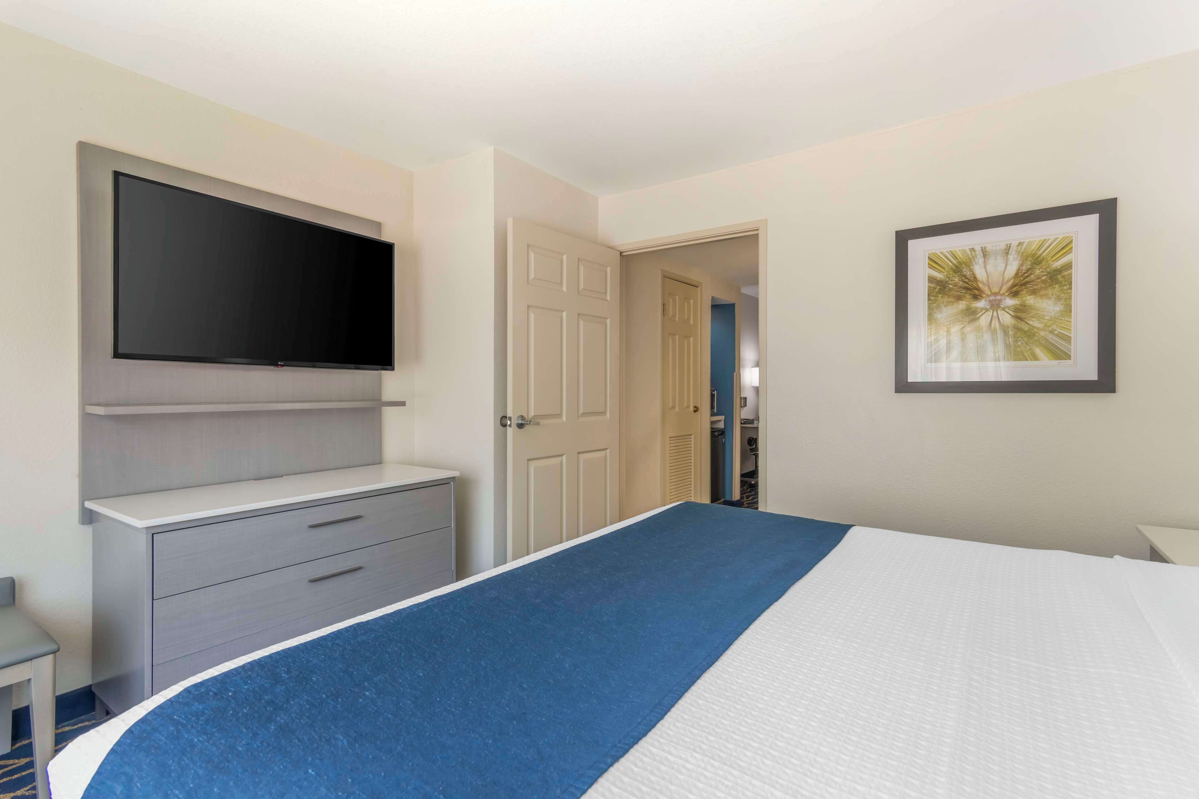 Habitación de hotel con una cama grande, un televisor de pantalla plana en la pared, un aparador y un cuadro enmarcado.