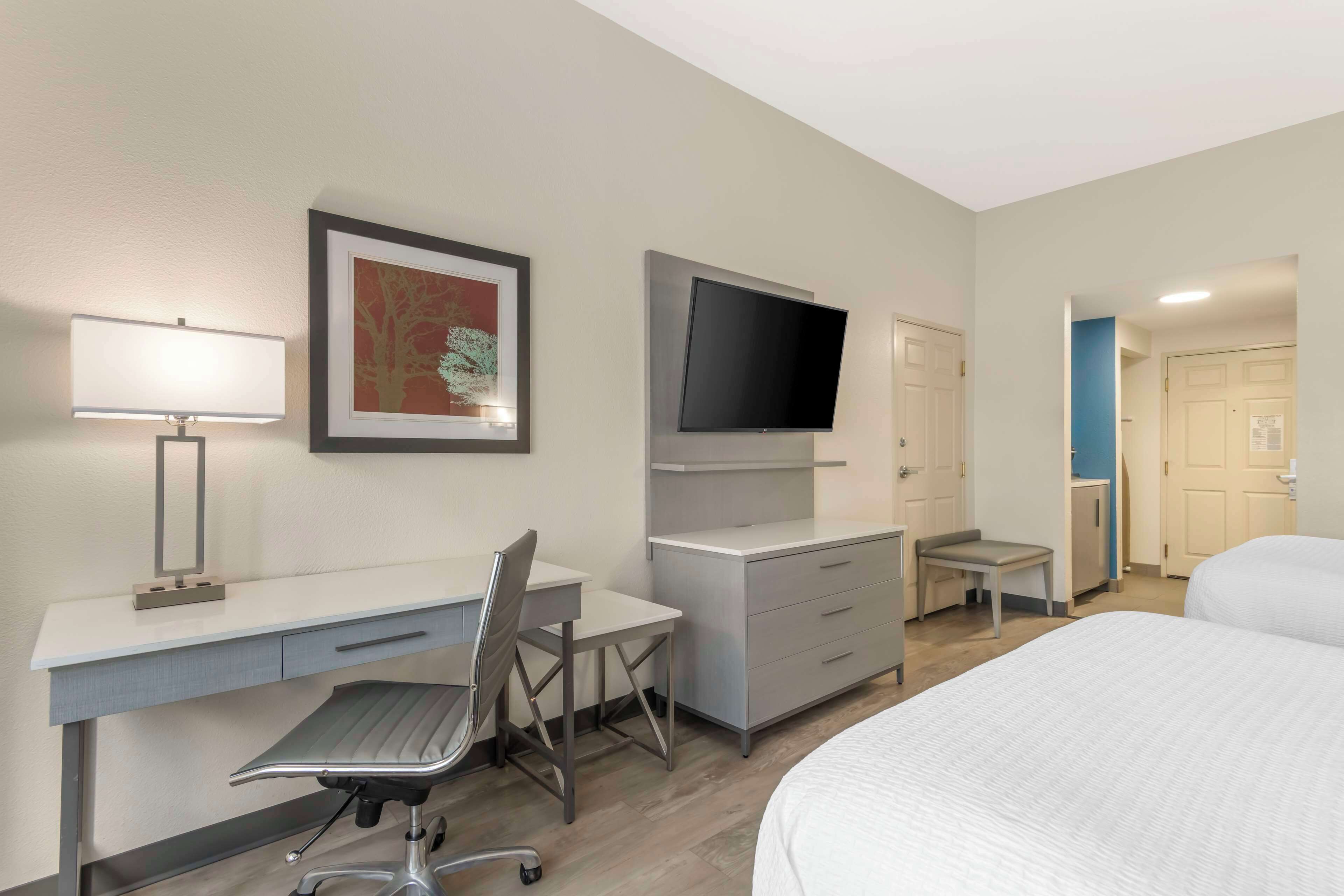 A hotel room with a bed, desk, chair, TV, and a small table.