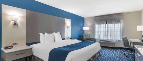 A hotel room with a large bed, a desk, a chair, and a window with curtains.