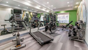 Un gimnasio con cintas de correr, máquinas de pesas y un espejo grande.