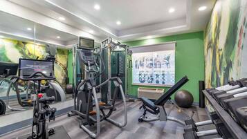 A gym with exercise equipment, a mirrored wall, and a green wall with a poster.